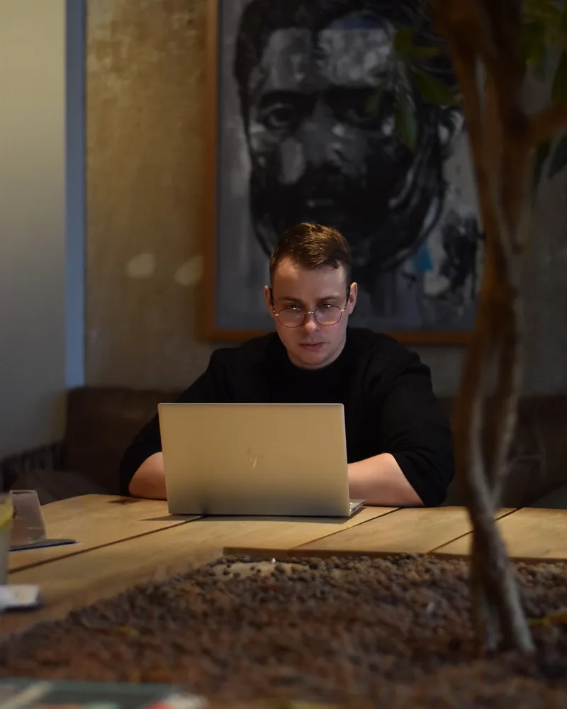 Christopher Krassnig at a table with a laptop, a dark painting behind him